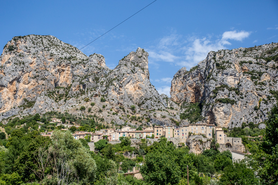 Vue sur le village perché de Moustiers -Sainte-Marie niché au pied de ses hautes falaises rocheuses sous un ciel bleu à proximité du camping Verdon Terra Verdon - Ciela Village à Castellane dans les Alpes-de-Haute-Provence