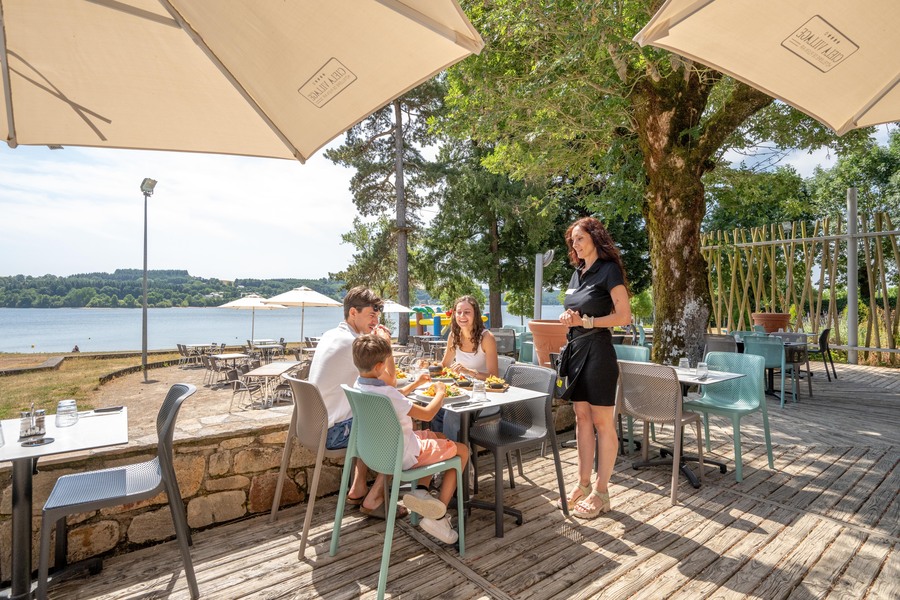 Famille qui déjeune sur la terrasse du restaurant avec vue sur lac de Pareloup au Camping Le Caussanel - Ciela Village à Canet-de-Salars dans l'Aveyron