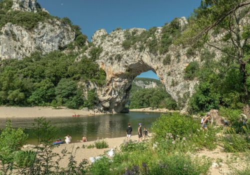L'arche naturelle du Pont d'Arc et sa rivière avec vacanciers faisant du canoë et d'autres sur la plage à proximité du camping Le Pommier - Ciela Village à Villeneuve de Berg en Ardèche