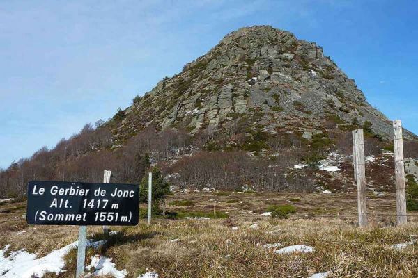 Vue sur le dôme rocheux du Mont Gerbier de Jonc, célèbre suc volcanique d'Ardèche, avec des restes de neige au sol et son panneau d'altitude au premier plan à proximité du camping Le Pommier - Ciela Village à Villeneuve de Berg en Ardèche
