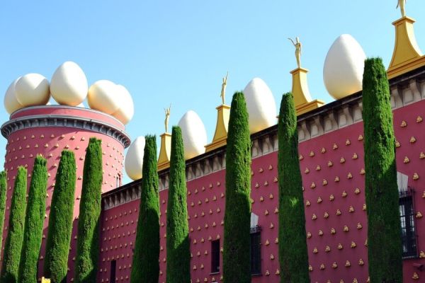 La façade rouge du Théâtre-Musée Salvador Dalí à Figueres, surmontée d'œufs géants et bordée de cyprès sous un ciel bleu à proximité du camping Les Marsouins - Ciela Village à Argelès-sur-Mer en Occitanie