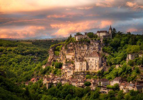 La cité médiévale de Rocamadour agrippée à sa falaise calcaire sous un ciel de coucher de soleil flamboyant dans le Lot à côté du camping Les Cigales - Ciela Village dans le Lot