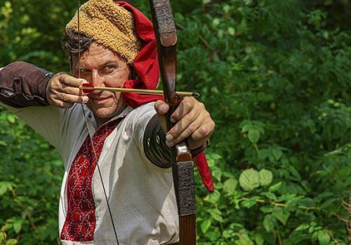 Gros plan d'un archer médiéval en costume d'époque dessinant son arc et visant avec une flèche au Parc Durandal à proximité du camping Les Cigales - Ciela Village dans le Lot
