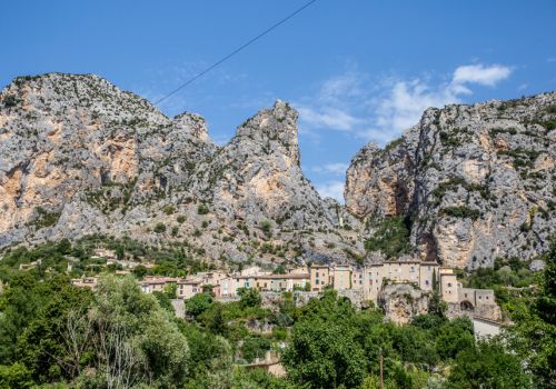 Vue sur le village perché de Moustiers -Sainte-Marie niché au pied de ses hautes falaises rocheuses sous un ciel bleu à proximité du camping Verdon Terra Verdon - Ciela Village à Castellane dans les Alpes-de-Haute-Provence