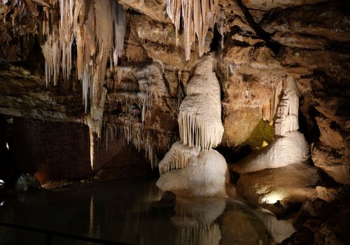 Concrétions calcaires, stalactites et stalagmites éclairées se reflétant dans l'eau souterraine des grottes de Lacave dans le Lot proche du camping les Cigales - Ciela Village
