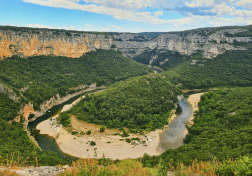 Vue panoramique sur le grand méandre de la rivière Ardèche entouré de hautes falaises calcaires et de forêts, avec des canoës visibles dans l'eau à proximité du camping Le Pommier - Ciela Village à Villeneuve de Berg en Ardèche
