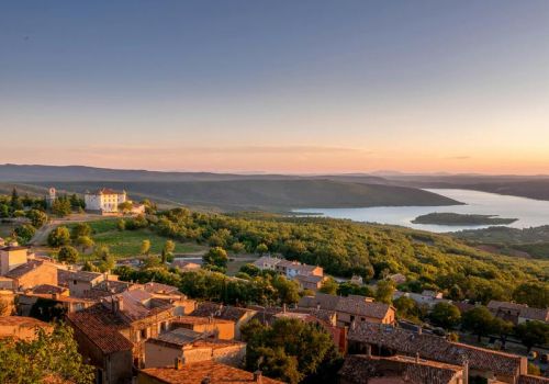 Vue panoramique au coucher de soleil sur le village d'Aiguines, avec château et lac à proxmité du camping Verdon Terra Verdon - Ciela Village à Castellane dans les Alpes-de-Haute-Provence