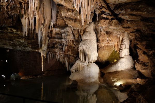 Concrétions calcaires, stalactites et stalagmites éclairées se reflétant dans l'eau souterraine des grottes de Lacave dans le Lot proche du camping les Cigales - Ciela Village