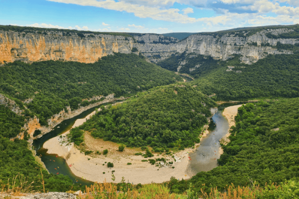 Vue panoramique sur le grand méandre de la rivière Ardèche entouré de hautes falaises calcaires et de forêts, avec des canoës visibles dans l'eau à proximité du camping Le Pommier - Ciela Village à Villeneuve de Berg en Ardèche