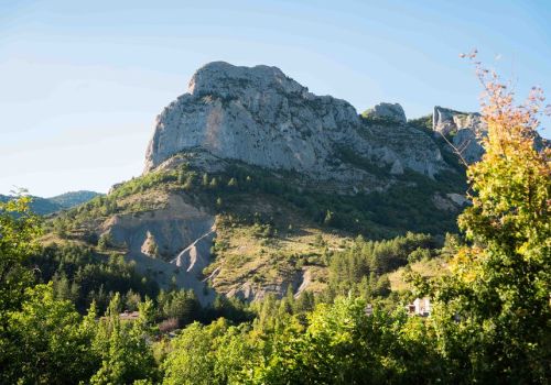 Vue depuis le camping Les Princes d'Orange Ciela Village sur le grand sommet rocheux escarpé à Orpierre dans les Hautes-Alpes, surplombant une forêt sous un ciel bleu ensoleillé