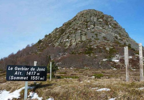 Vue sur le dôme rocheux du Mont Gerbier de Jonc, célèbre suc volcanique d'Ardèche, avec des restes de neige au sol et son panneau d'altitude au premier plan à proximité du camping Le Pommier - Ciela Village à Villeneuve de Berg en Ardèche