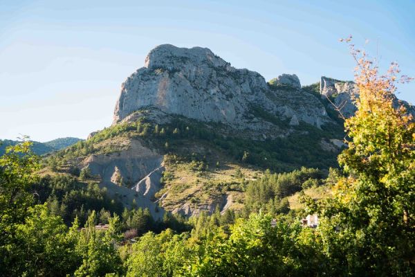 Vue depuis le camping Les Princes d'Orange Ciela Village sur le grand sommet rocheux escarpé à Orpierre dans les Hautes-Alpes, surplombant une forêt sous un ciel bleu ensoleillé